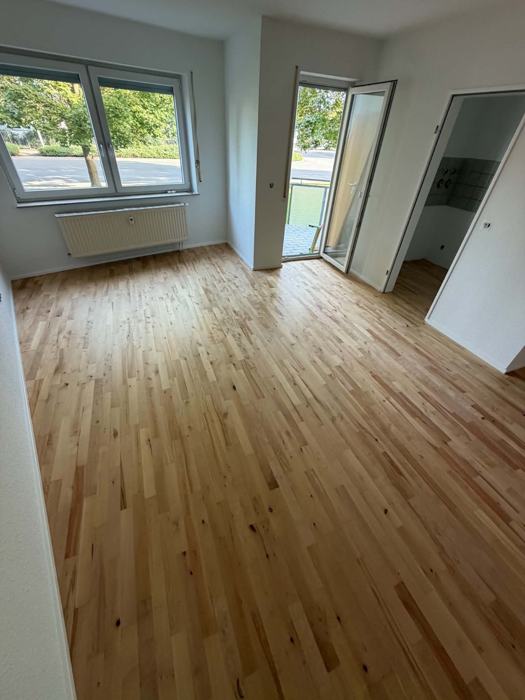 Wohnraum mit hellem Stabparkett und Balkontür